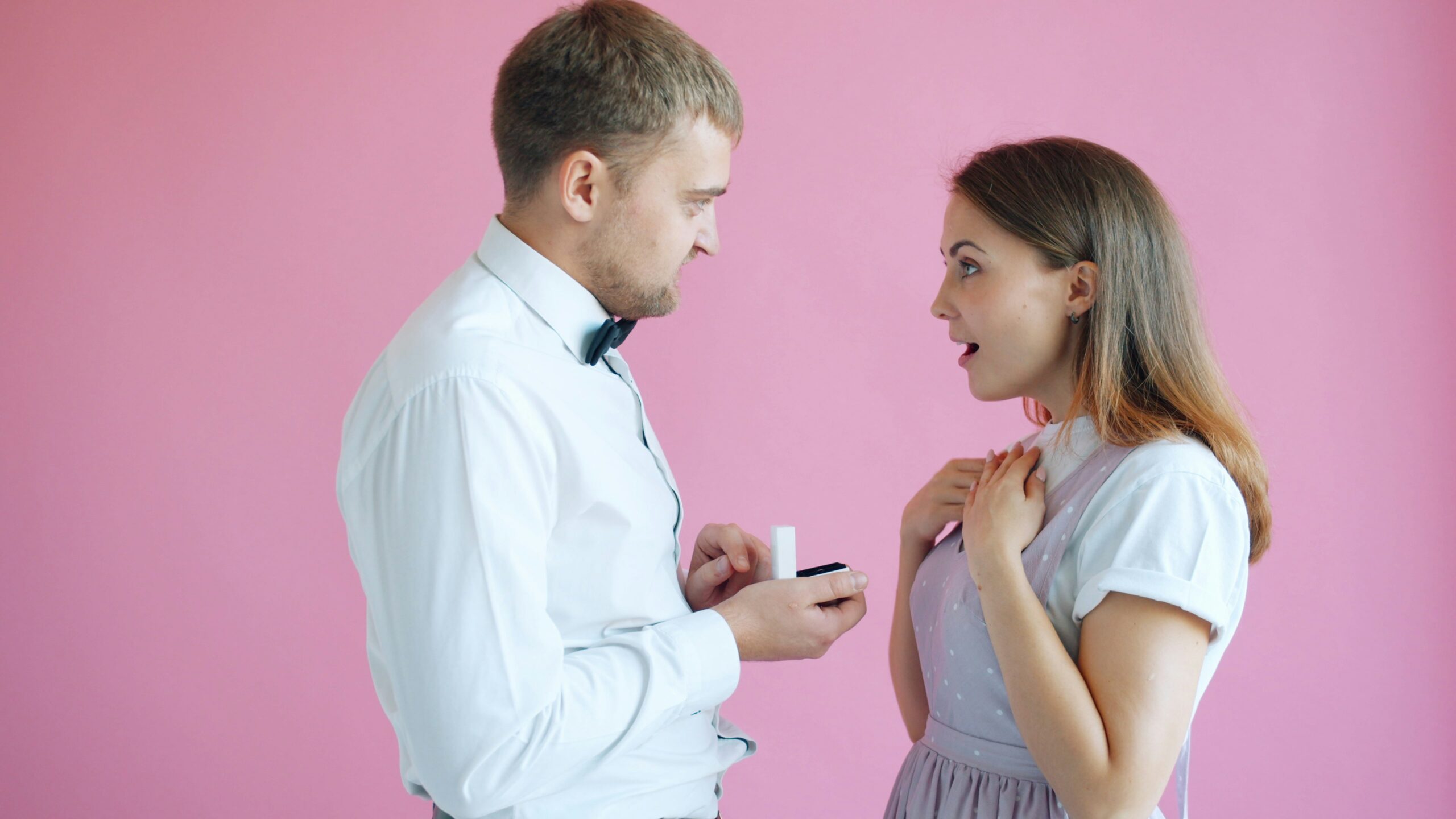 Couple debout célébrant la Saint-Valentin, l’homme montrant une bague de fiançailles.