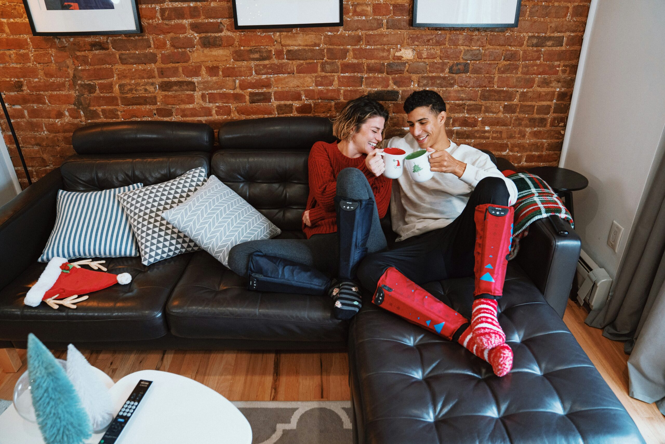 Couple en chaussettes de Noël trinquant sur un canapé pour une Saint-Valentin simple et cosy.