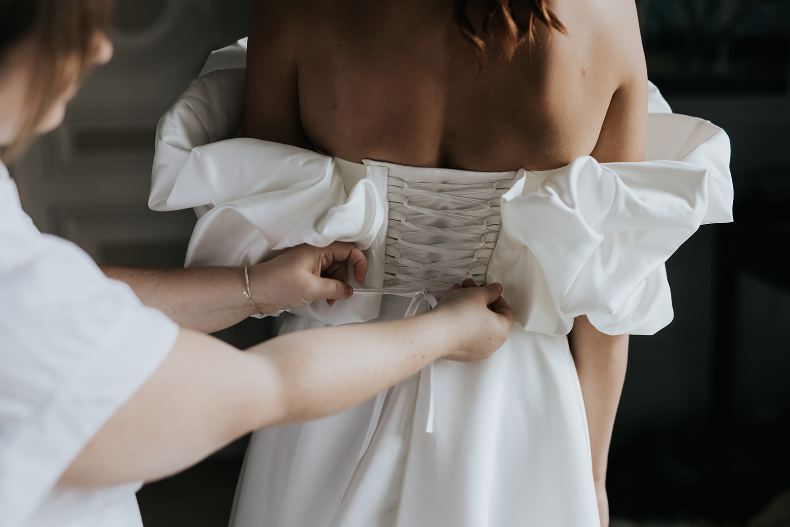 Wedding planner aidant la mariée à enfiler sa robe le jour J
