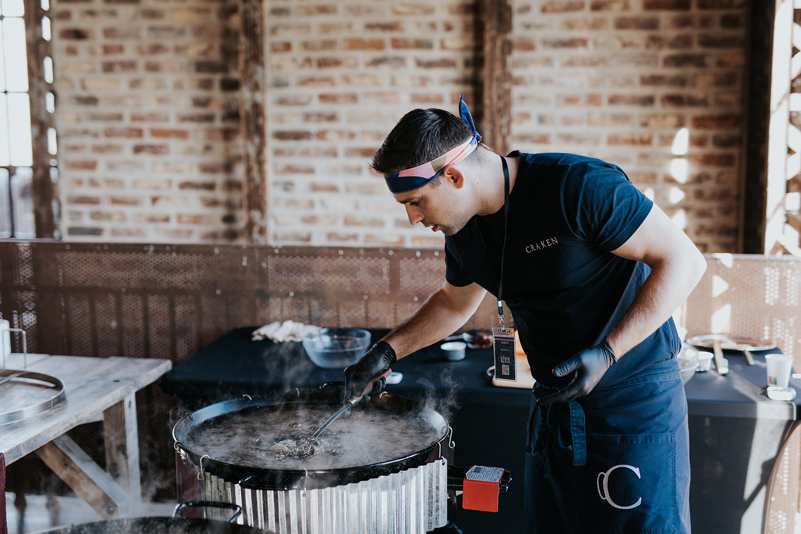 Chef cuisinant dans une grande poêle fumante dans un espace industriel en briques