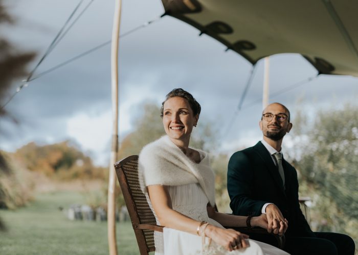 Couple de mariés assis sous un voile de tente lors d'une cérémonie en plein air en automne